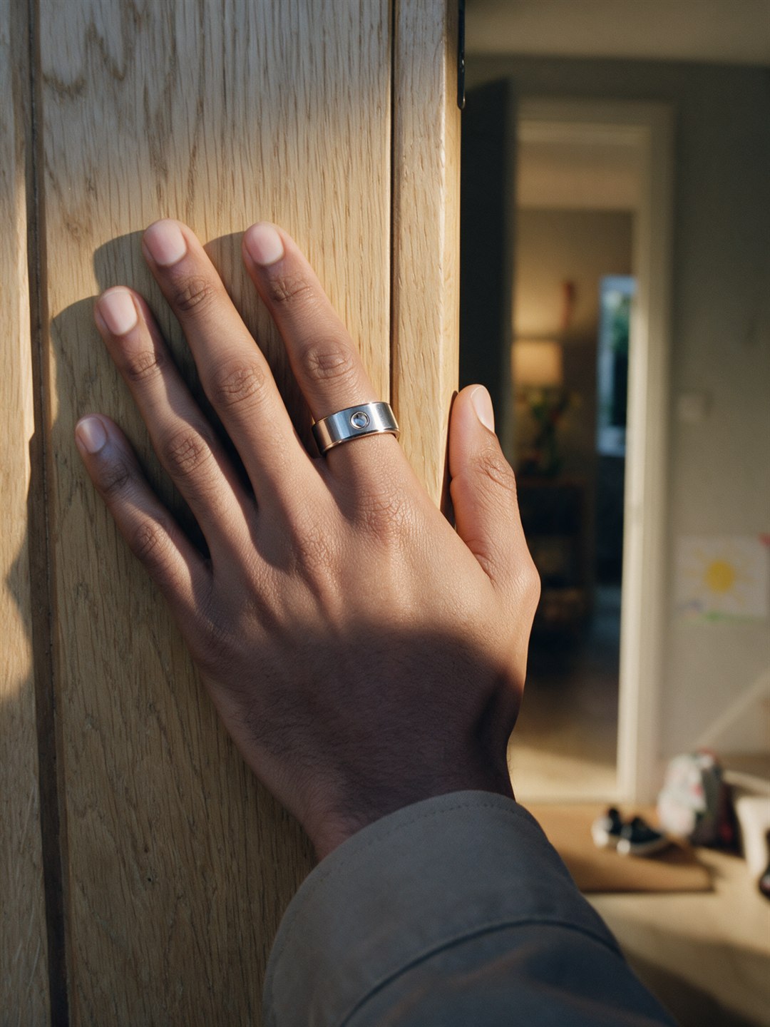Generated image: a man's left hand easing his front door open in evening sun, the ring on his index finger, a warm family hallway beyond with a child's drawing and small trainers